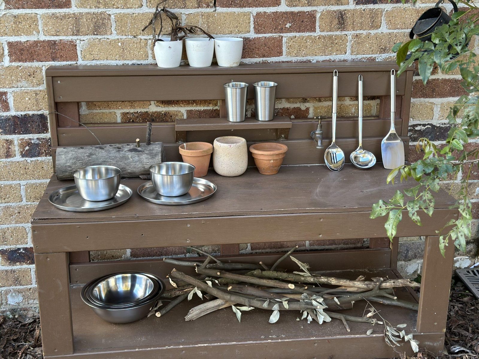 Mud kitchen shelf stacked with tins, cups and spoons