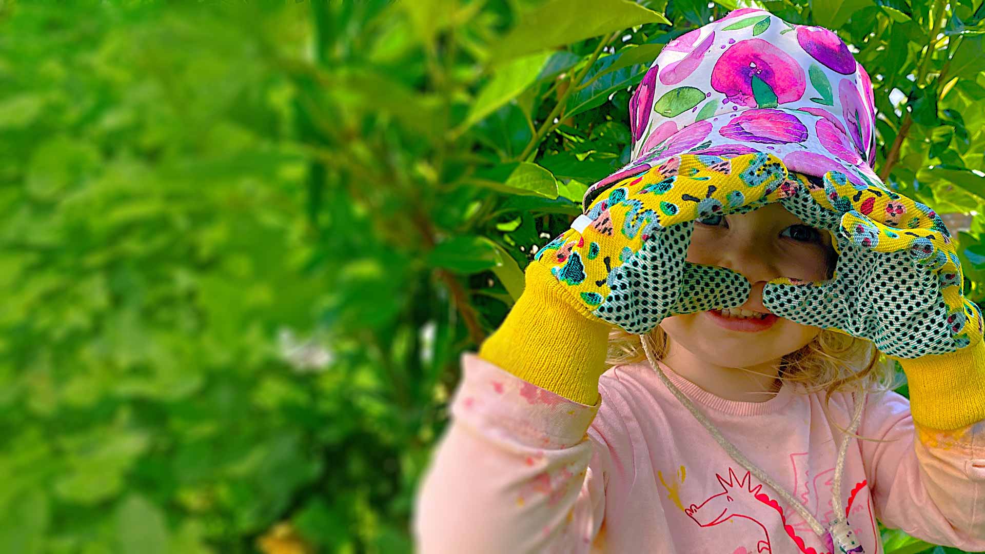 A child smiling among lush green leaves at Currumbin Village Early Learning